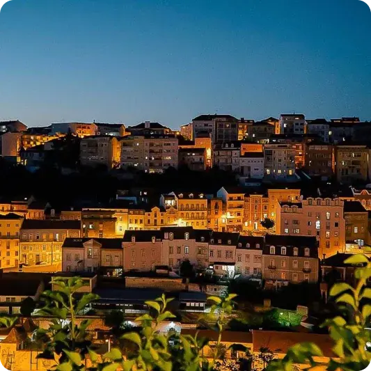 Casas iluminadas numa colina de Coimbra ao anoitecer, vistas do terraço