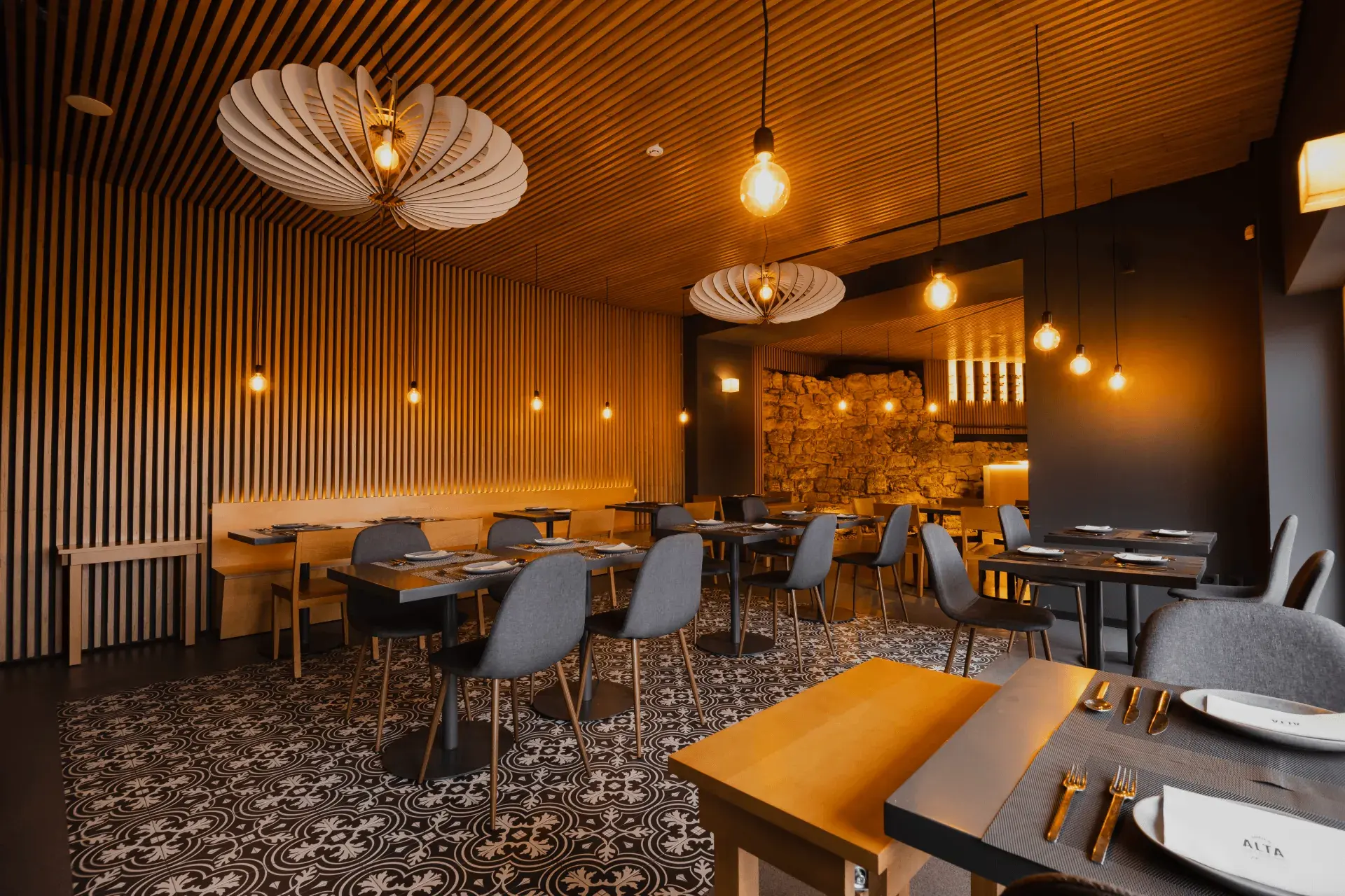 Sala interior do restaurante com teto e paredes de ripas de madeira, candeeiros suspensos e parte da antiga muralha de Coimbra ao fundo